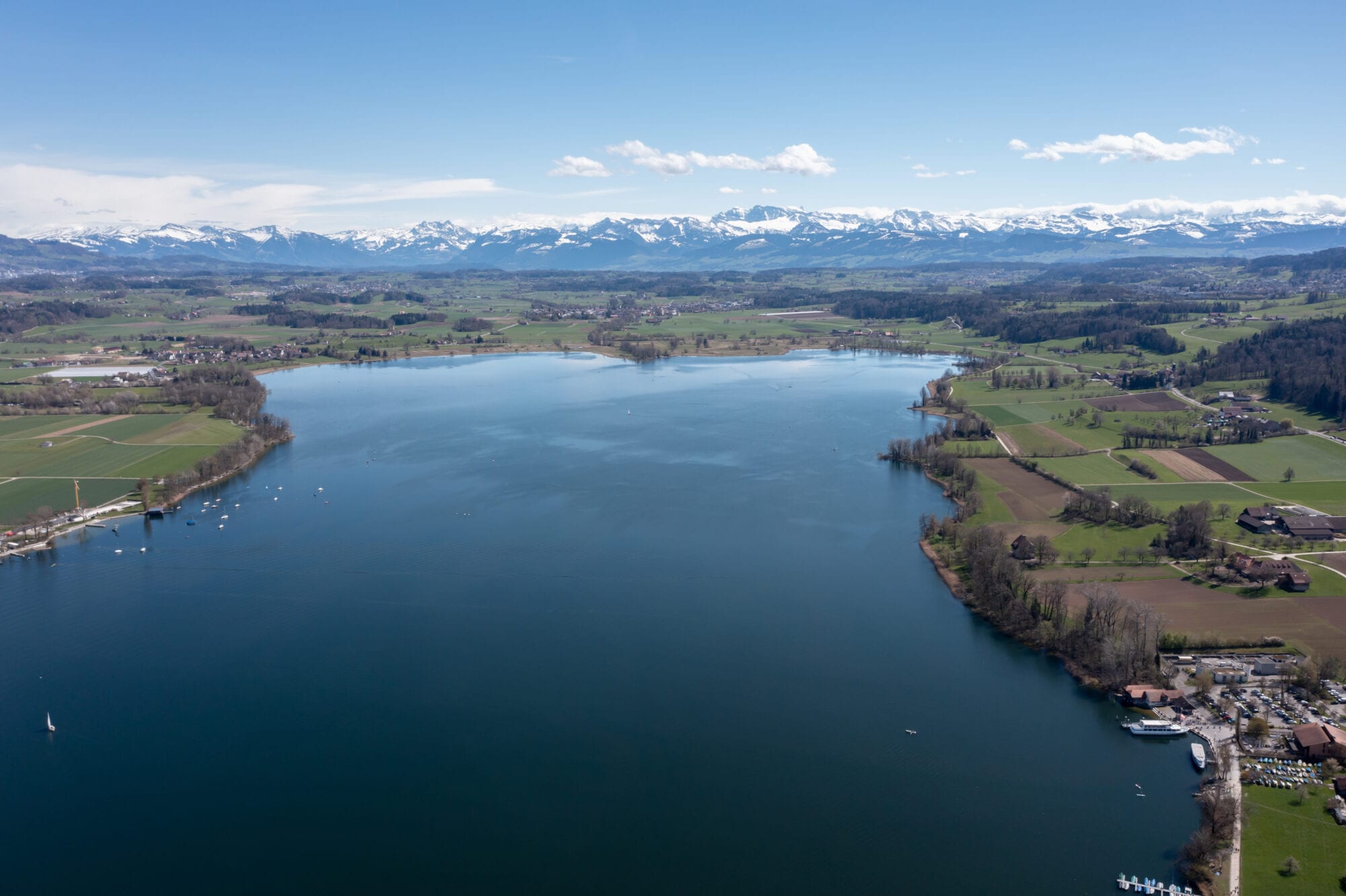 Luftaufnahme vom Greifensee im Vordergrund und den schneebedeckten Bergen der Alpen im Hintergrund, Zürich, Schweiz