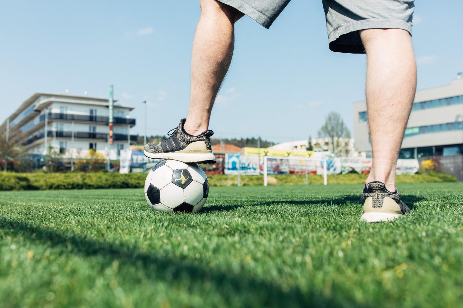Zwei Beine eines Mannes, der mit seinem linken Fuß auf einem Fußball auf einem Sportplatz steht