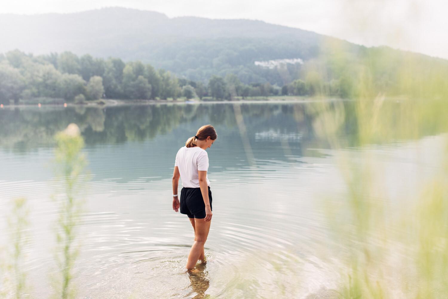 Eine Frau von hinten ist mit ihren Füßen in einem See und schaut dabei nach unten