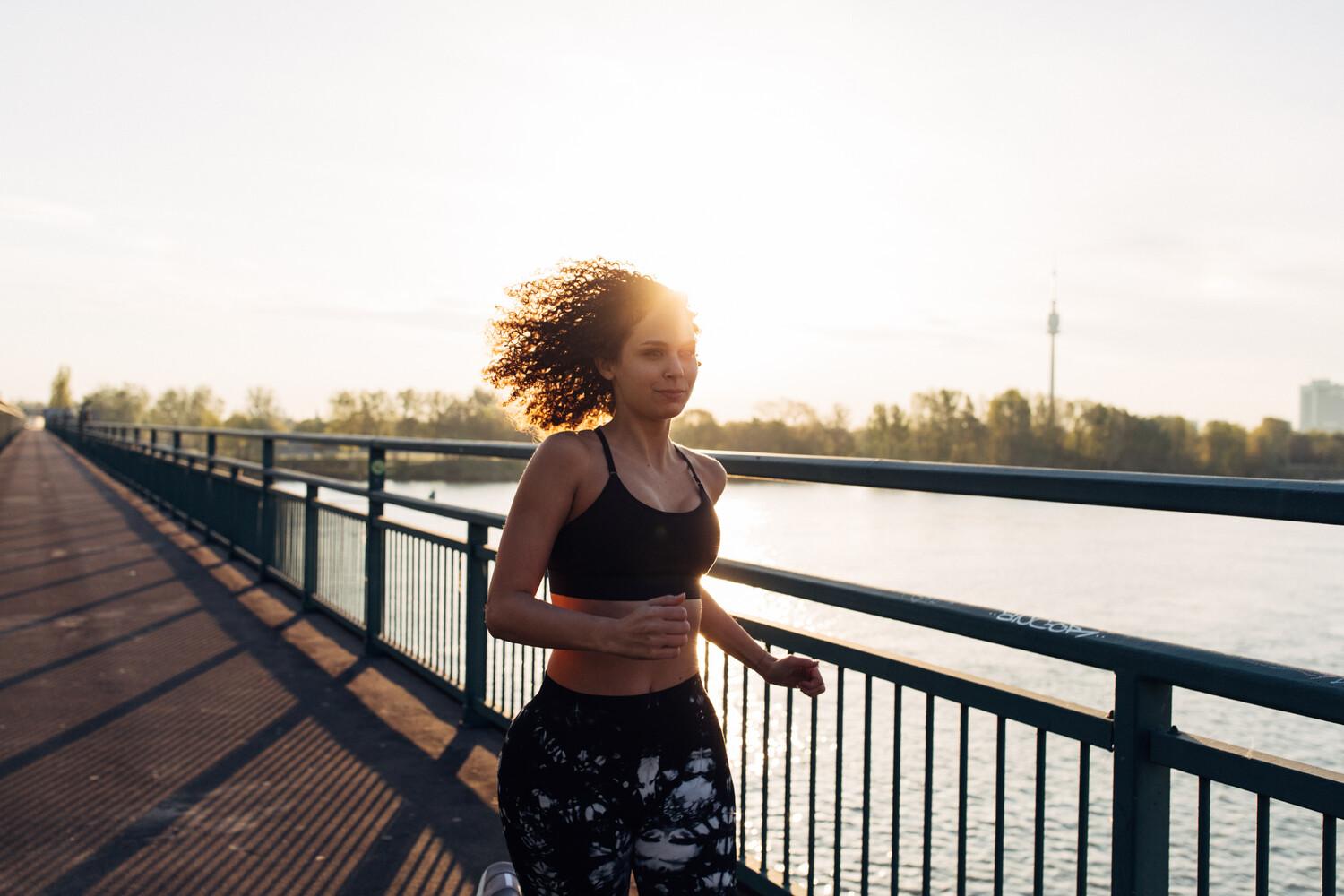 Eine Frau joggt bei Sonnenschein einen Weg an einem Fluss entlang