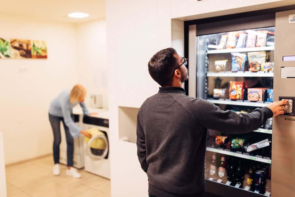 Zwei Personen im service point, ein Mann am Snackautomaten, eine Frau an der Waschmaschine