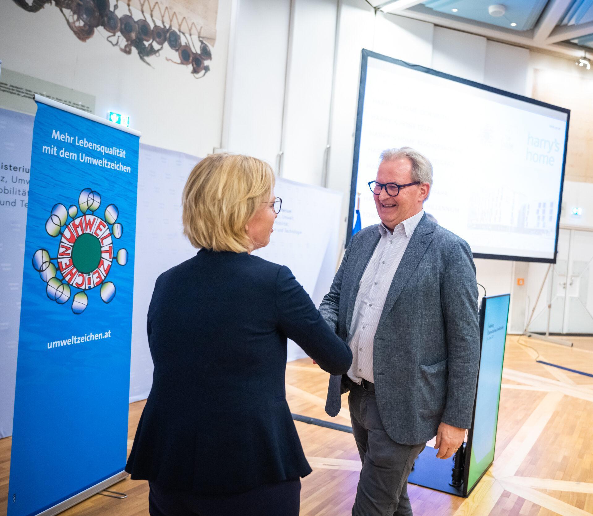 Leonore Gewessler schüttelt Gründer Harald Ultsch bei einer Veranstaltung lächelnd die Hand