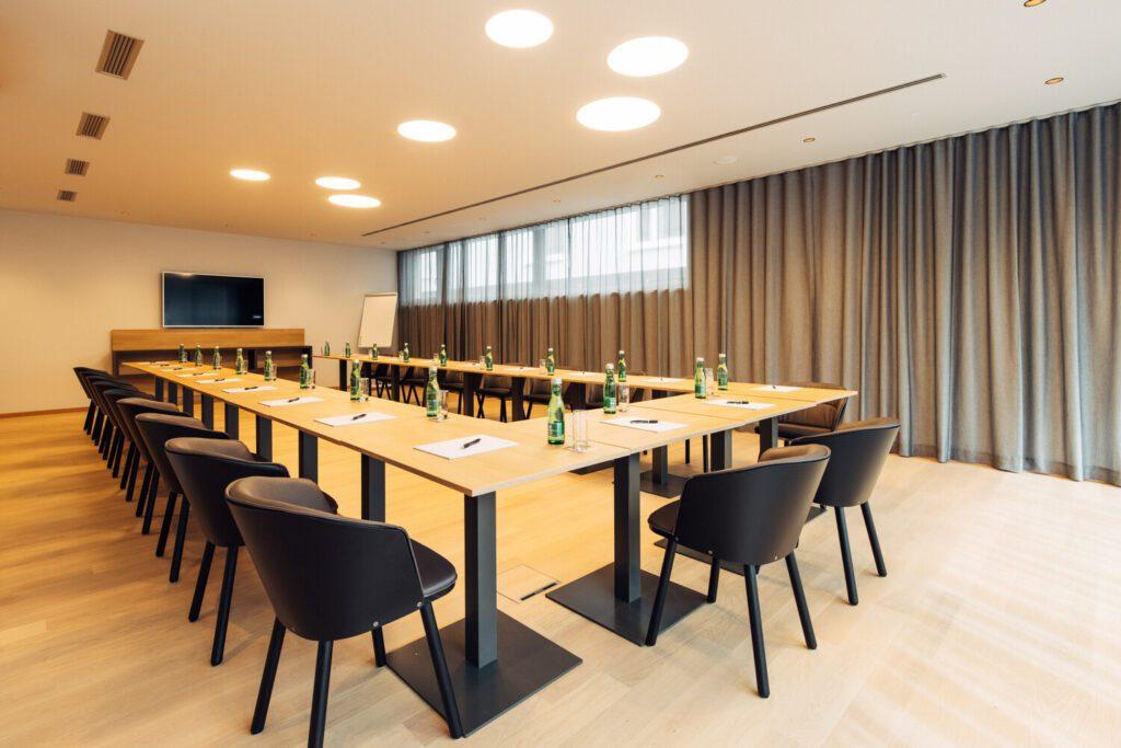 Großer Konferenzraum für Business-Meetings mit u-förmiger Tischanordnung und schwarzen Stühlen